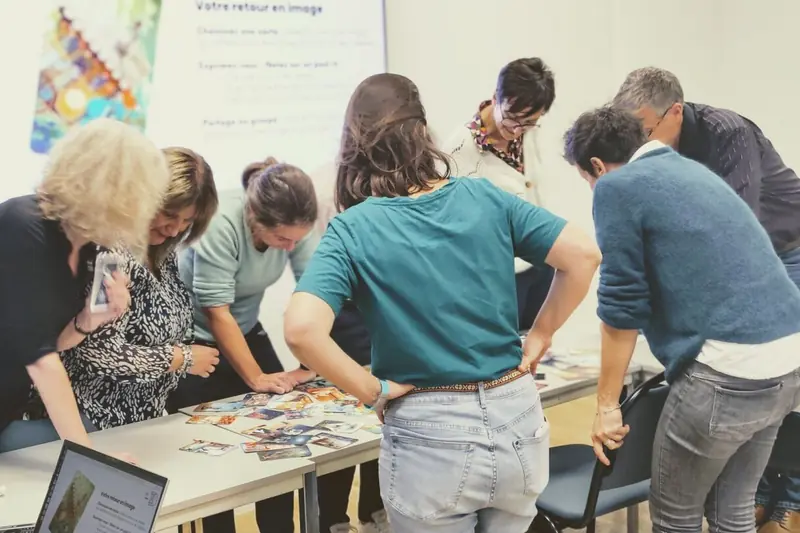 Des participants penchés sur une table couverte de cartes illustrées, pendant un temps de retour en image